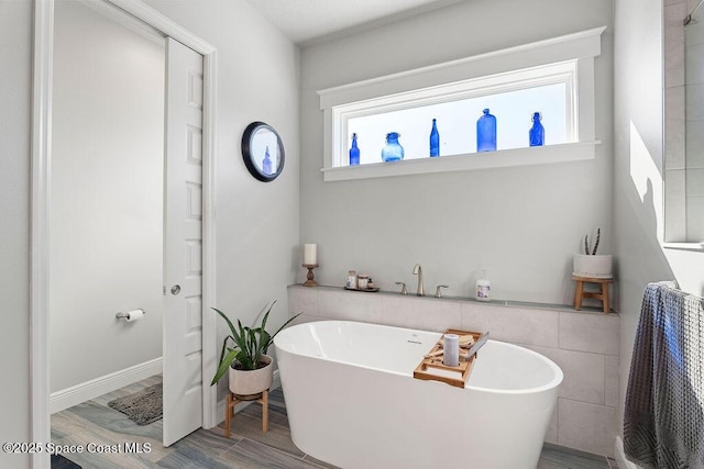 full bath with wood finished floors, tile walls, and a freestanding tub