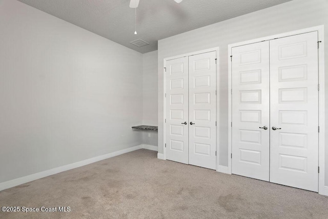 unfurnished bedroom featuring visible vents, two closets, a textured ceiling, carpet flooring, and baseboards