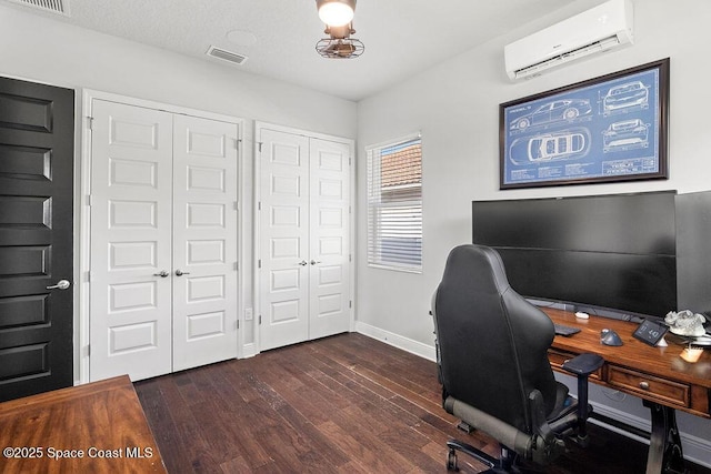 home office with visible vents, an AC wall unit, dark wood-type flooring, and baseboards