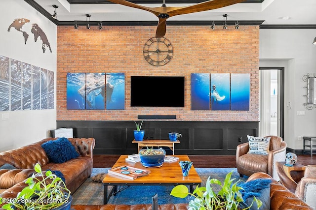 living room featuring rail lighting, wood finished floors, brick wall, and ornamental molding