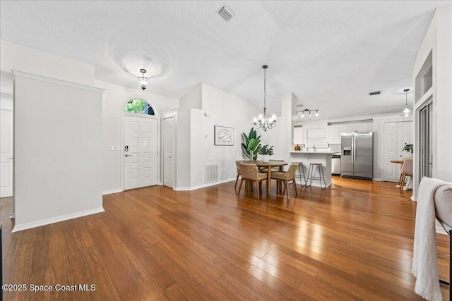 entrance foyer featuring visible vents, a textured ceiling, hardwood / wood-style floors, and a chandelier