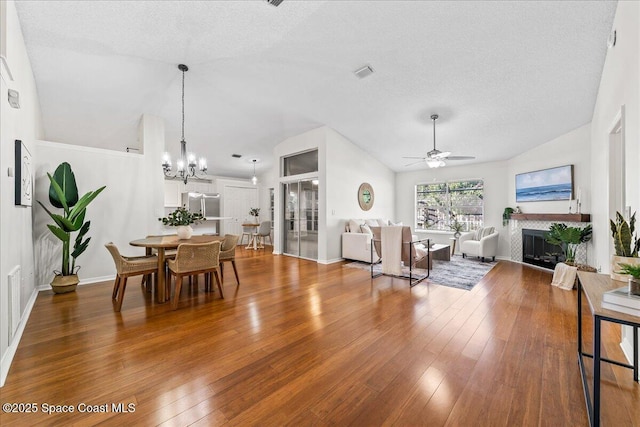 living area with visible vents, ceiling fan with notable chandelier, wood-type flooring, a fireplace, and lofted ceiling