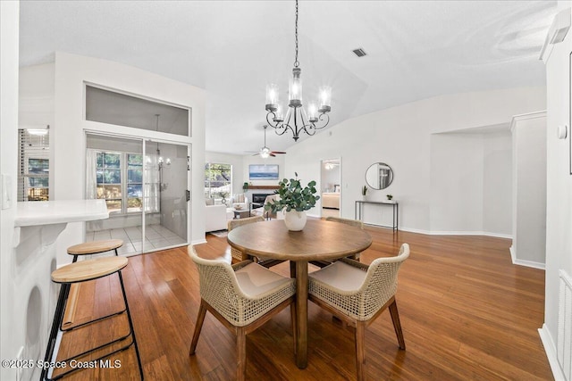 dining space with wood finished floors, visible vents, baseboards, lofted ceiling, and a fireplace