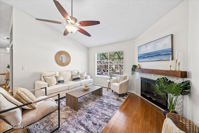 living room featuring ceiling fan, a tiled fireplace, lofted ceiling, hardwood / wood-style flooring, and a textured ceiling