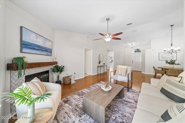 living area featuring wood finished floors, visible vents, baseboards, a fireplace, and ceiling fan with notable chandelier