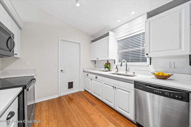 kitchen with a sink, stainless steel appliances, light countertops, white cabinets, and light wood-style floors