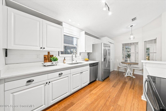 kitchen featuring visible vents, lofted ceiling, appliances with stainless steel finishes, white cabinetry, and a sink