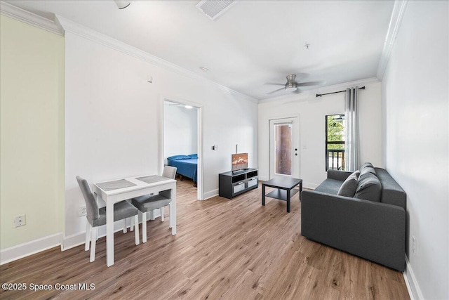 living room featuring visible vents, crown molding, baseboards, ceiling fan, and light wood-style flooring