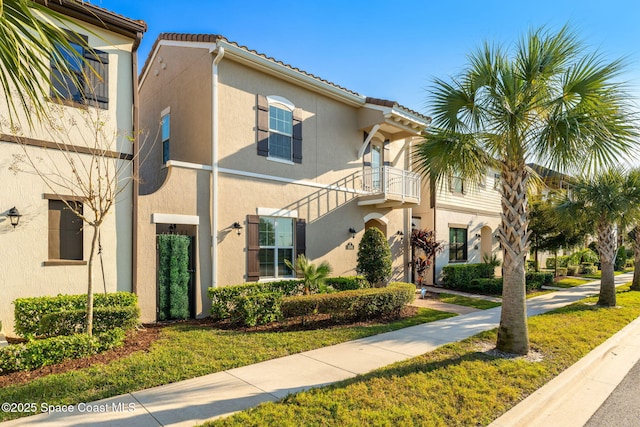 view of front of home with a balcony, a tiled roof, and stucco siding