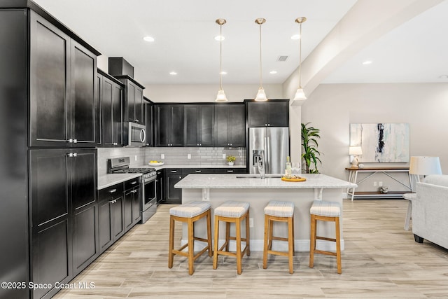 kitchen with decorative backsplash, dark cabinets, appliances with stainless steel finishes, and a breakfast bar