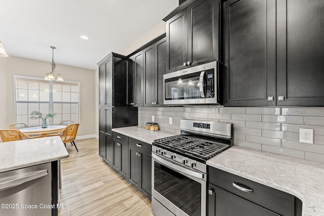 kitchen featuring light wood finished floors, stainless steel appliances, tasteful backsplash, and dark cabinets