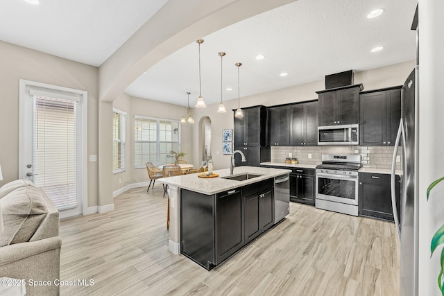 kitchen with a sink, open floor plan, dark cabinetry, stainless steel appliances, and arched walkways