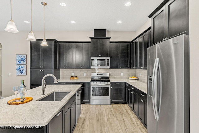 kitchen featuring dark cabinets, stainless steel appliances, light wood-style floors, and a sink