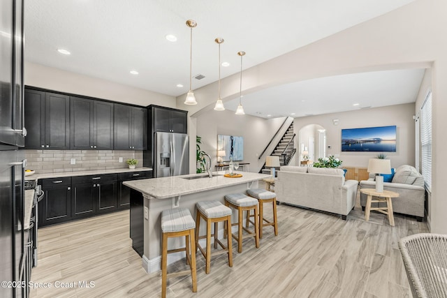 kitchen with open floor plan, dark cabinets, a kitchen breakfast bar, stainless steel fridge, and a sink