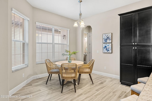 dining room with baseboards, arched walkways, and light wood finished floors