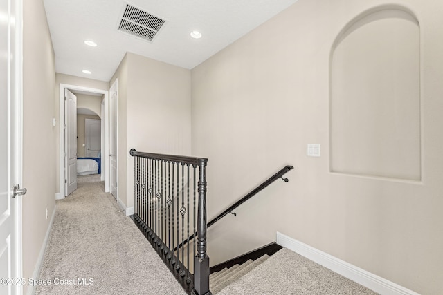 corridor with visible vents, an upstairs landing, arched walkways, carpet floors, and baseboards