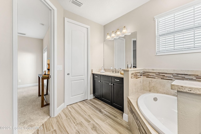 full bath featuring visible vents, baseboards, wood finished floors, a bath, and vanity