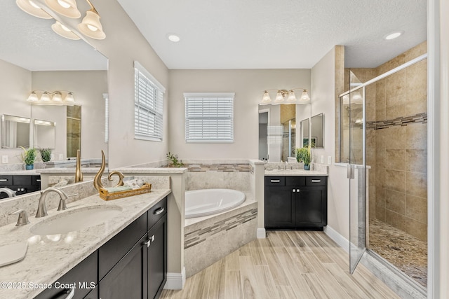 bathroom featuring two vanities, a stall shower, a sink, a textured ceiling, and a garden tub