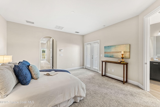 bedroom featuring arched walkways, visible vents, light carpet, and baseboards