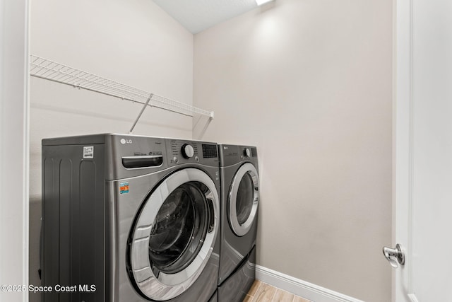 laundry area featuring laundry area, light wood-style flooring, washing machine and dryer, and baseboards