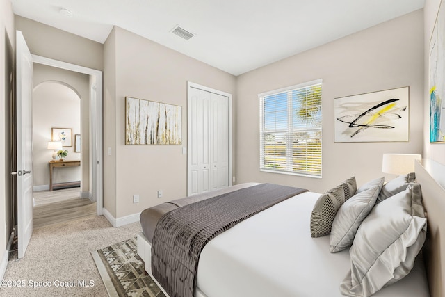 bedroom with visible vents, light carpet, a closet, arched walkways, and baseboards