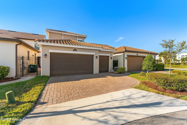 view of front of property with a gate, stucco siding, a garage, a tiled roof, and decorative driveway