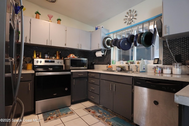 kitchen with a sink, backsplash, stainless steel appliances, light tile patterned flooring, and light countertops