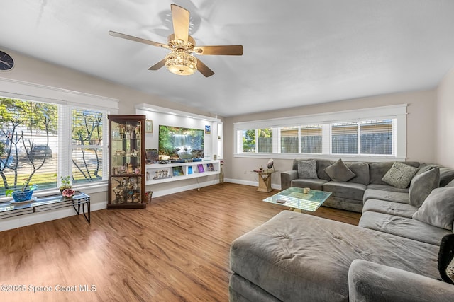 living area featuring wood finished floors, baseboards, and a ceiling fan