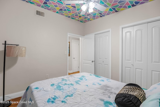 bedroom with baseboards, wood finished floors, multiple closets, and visible vents