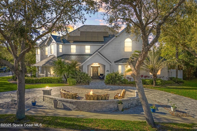 traditional-style house with roof mounted solar panels, curved driveway, and an outdoor fire pit