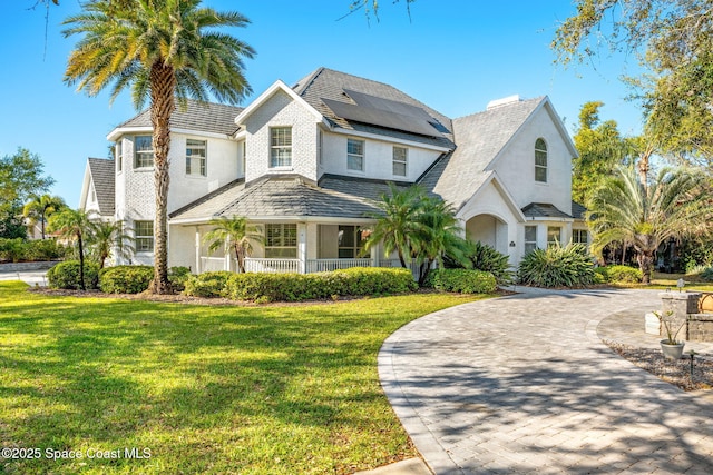 view of front of house featuring curved driveway, solar panels, a front yard, stucco siding, and a chimney