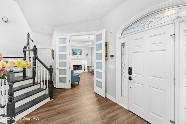 foyer entrance featuring a brick fireplace, baseboards, stairway, wood finished floors, and a textured ceiling