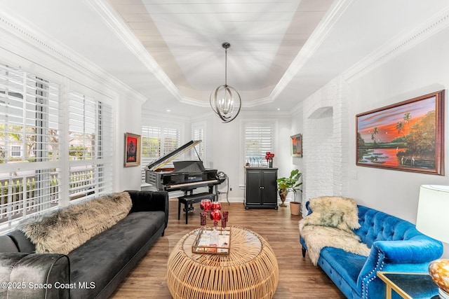 living area with wood finished floors, baseboards, an inviting chandelier, a tray ceiling, and crown molding