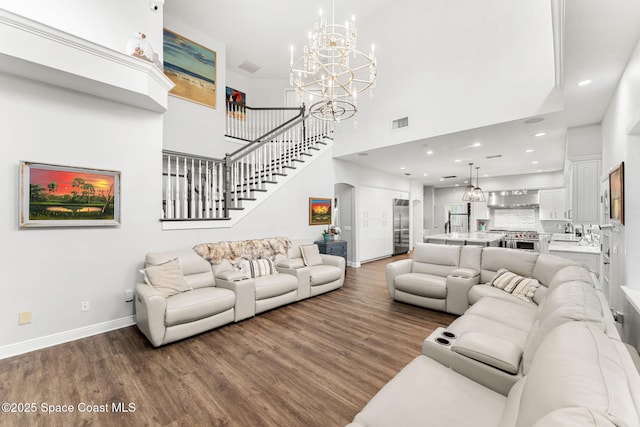 living area featuring visible vents, baseboards, a chandelier, a high ceiling, and wood finished floors