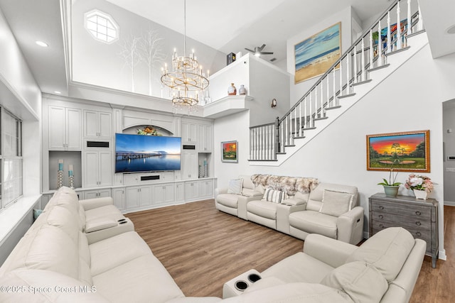 living room featuring a high ceiling, wood finished floors, stairs, and ceiling fan with notable chandelier