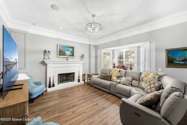 living room featuring a textured ceiling, wood finished floors, crown molding, a brick fireplace, and a chandelier