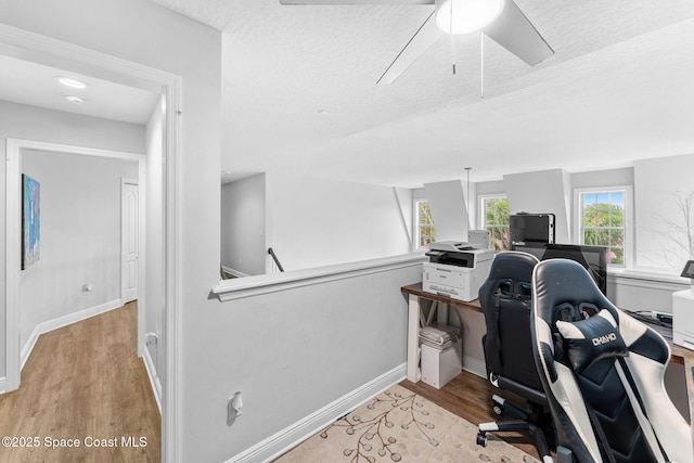 office area with a textured ceiling, baseboards, light wood-type flooring, and a ceiling fan