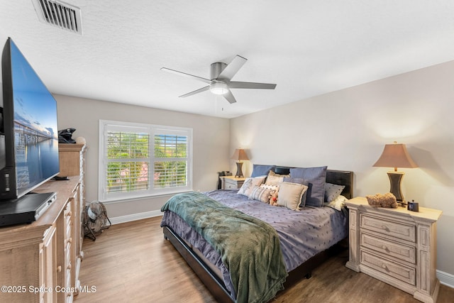 bedroom featuring visible vents, a ceiling fan, a textured ceiling, wood finished floors, and baseboards