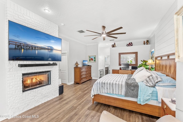 bedroom featuring visible vents, ornamental molding, wood finished floors, baseboards, and a brick fireplace