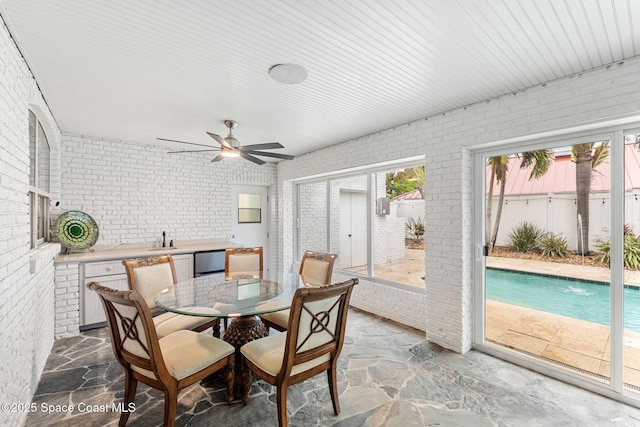 dining room with brick wall, stone flooring, and a ceiling fan