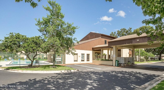 view of building exterior with a community pool, uncovered parking, and fence