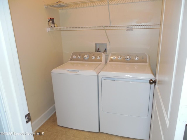 clothes washing area featuring laundry area, light tile patterned flooring, washing machine and dryer, and baseboards