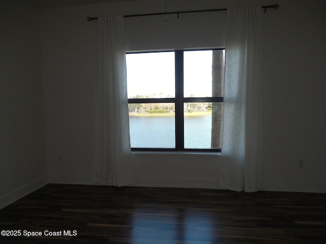 empty room featuring baseboards, a water view, and dark wood-style floors