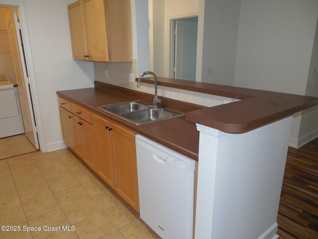 kitchen with a sink, dark countertops, a peninsula, washer / dryer, and dishwasher