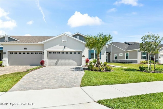 ranch-style home with decorative driveway, a front yard, an attached garage, and stucco siding