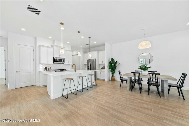kitchen featuring visible vents, appliances with stainless steel finishes, light countertops, an island with sink, and a breakfast bar area