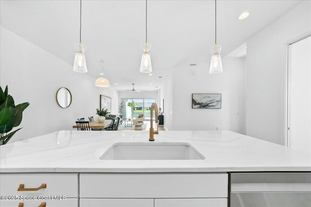 kitchen with white cabinets, open floor plan, a sink, and light stone counters