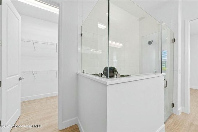 bathroom featuring a walk in closet, baseboards, wood finished floors, and a stall shower
