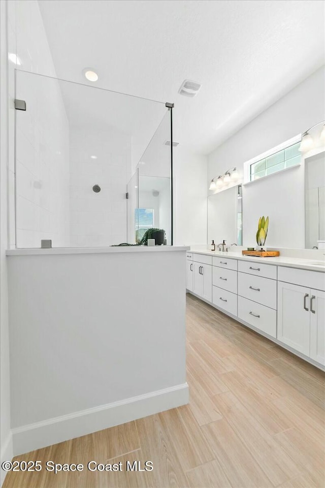 full bathroom with wood finished floors, a walk in shower, double vanity, baseboards, and visible vents