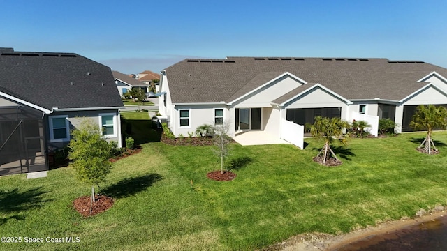 rear view of house with a lawn, a shingled roof, a lanai, and stucco siding